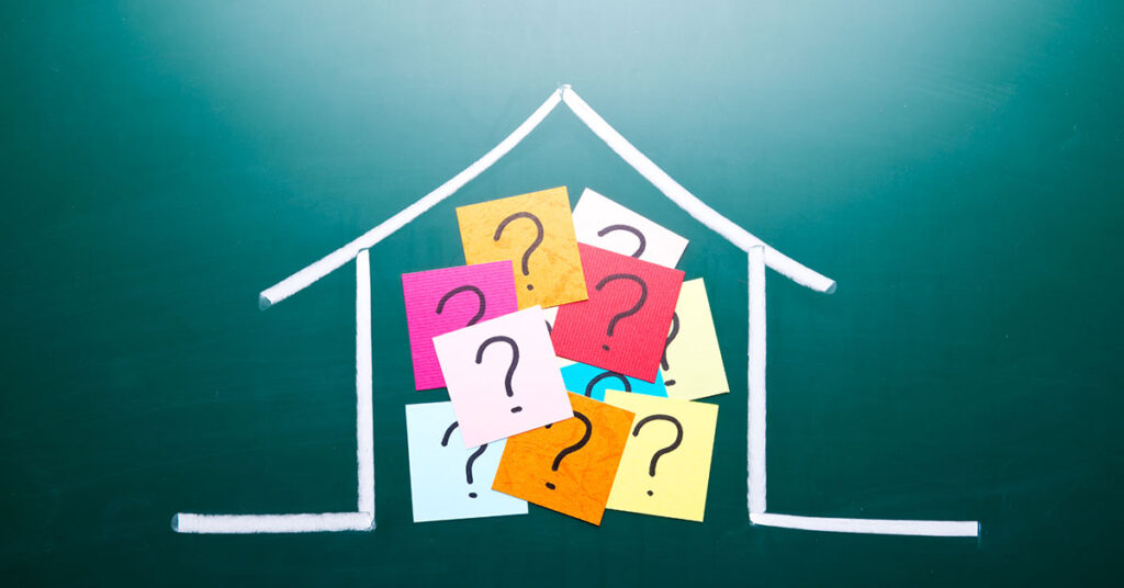 Ein Haus ist mit Kreide auf eine grüne Tafel gezeichnet und im Haus kleben Post-its mit Fragezeichen | Immobilienkauf